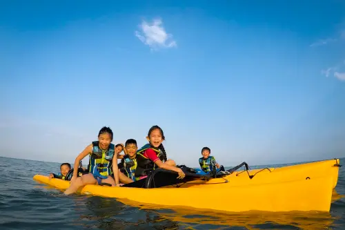 Kids in life jackets having fun on a yellow kayak in the ocean
