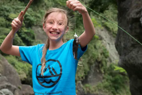Girl proudly holding up a fish caught with a handmade fishing rod