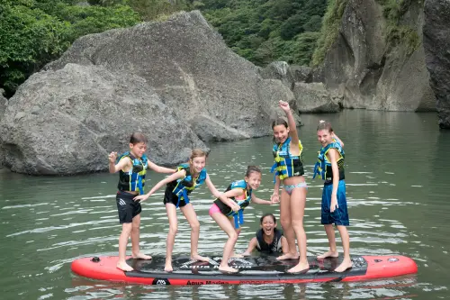 Group of campers standing on a giant paddle board in a river gorge